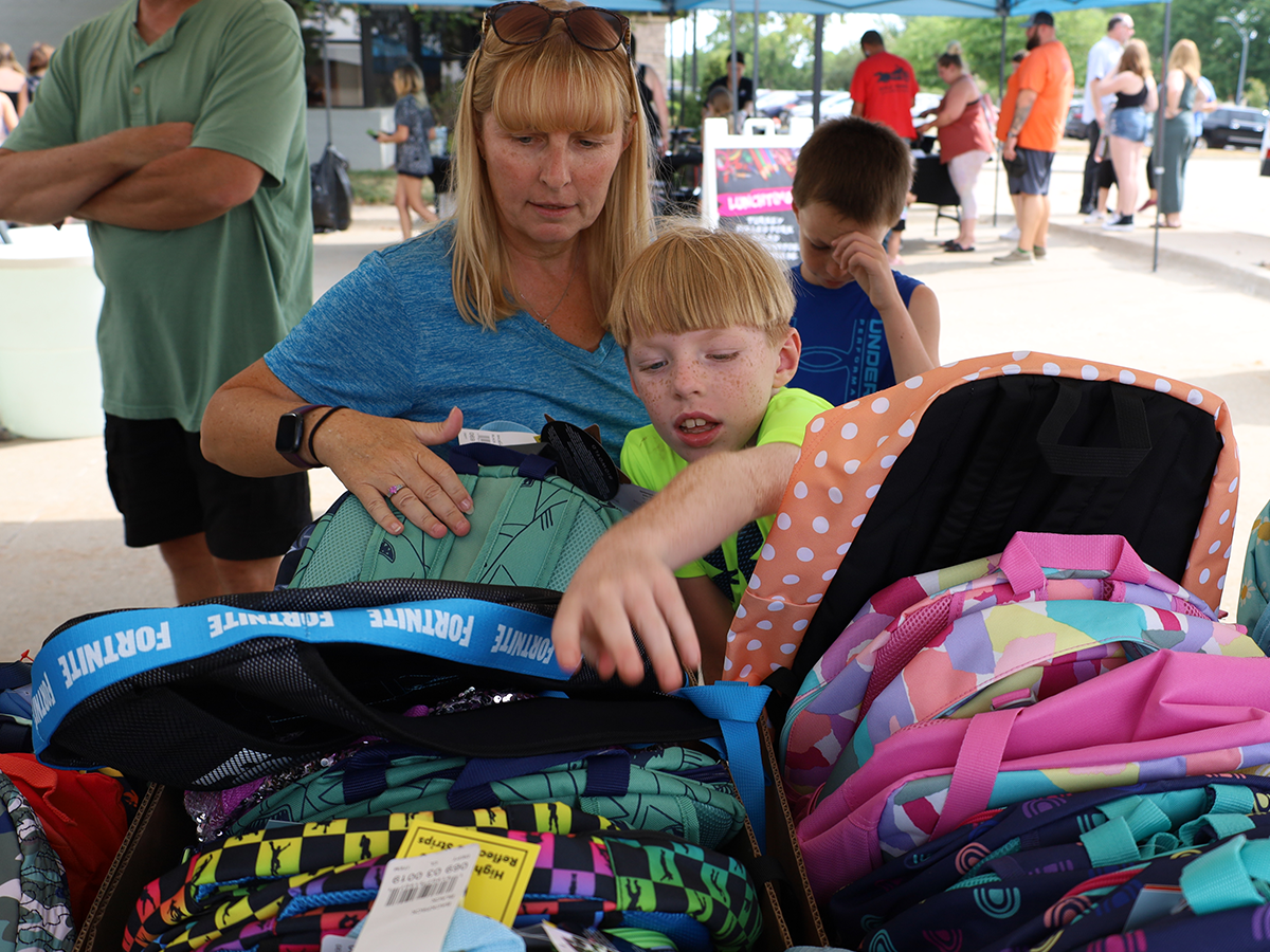 child and mom choosing backpack at back-to-school bash